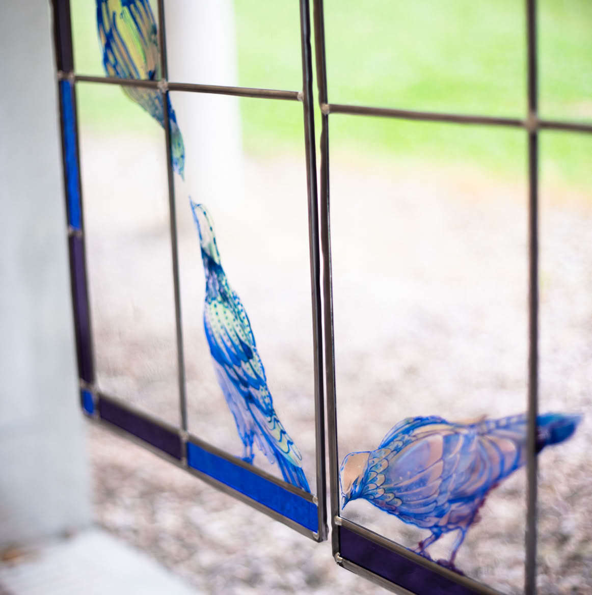 Stained glass window with blue bird designs, set against a blurred outdoor background.