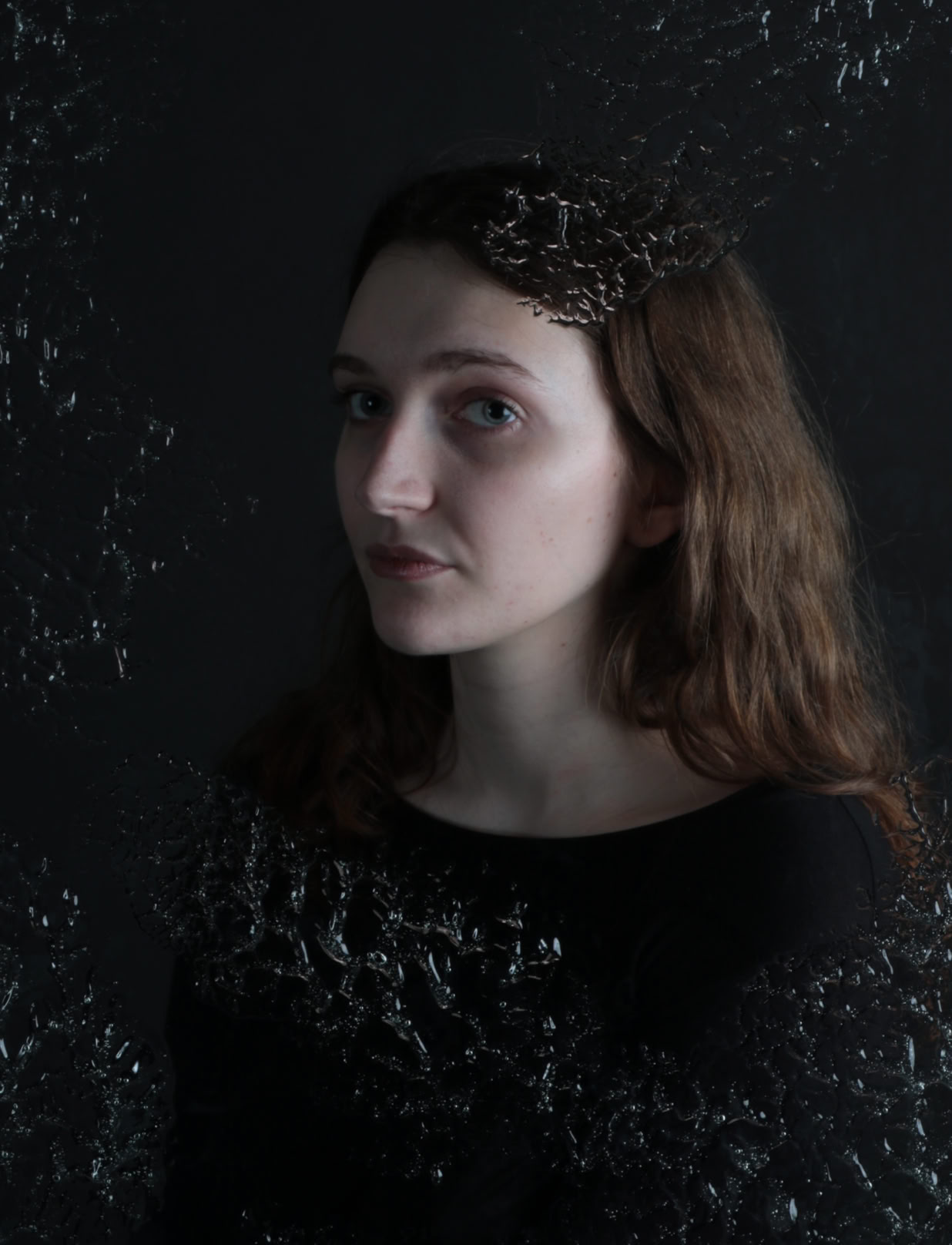 A person with long hair wearing a dark top, standing against a dark background with a textured overlay.